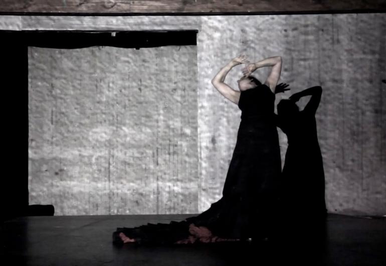 Video still from the preview of &quot;Love to Death (Amor a la muerte). A woman in a long dark gown arches her back with head back and up and bent in protective pose.