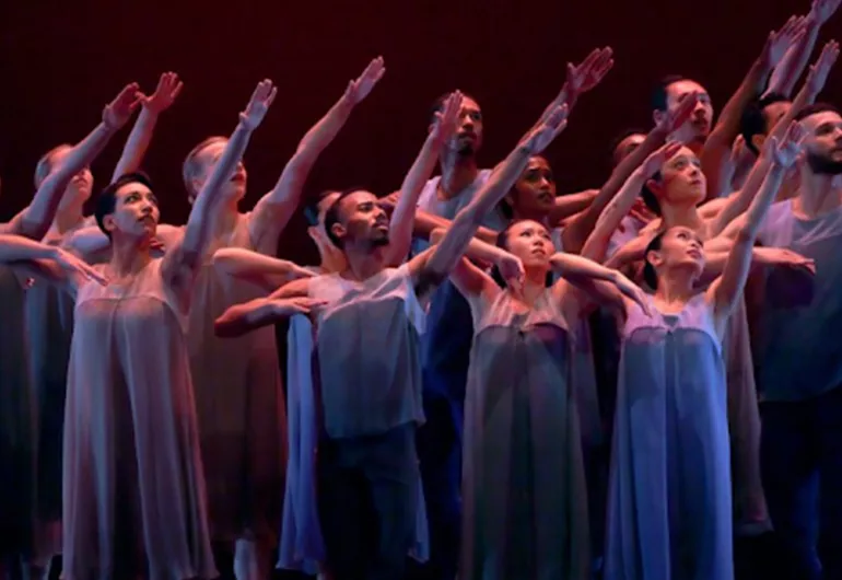 Fifteen dancers are shown in a colored image. The dancers are all lifting their left arm and looking towards it. Their right arm is bent at the elbow and raised. Some dancers are wearing dresses and others are wearing tops and pants.