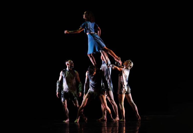 Group of dancer support another as she walks over their hands up high above there stage.