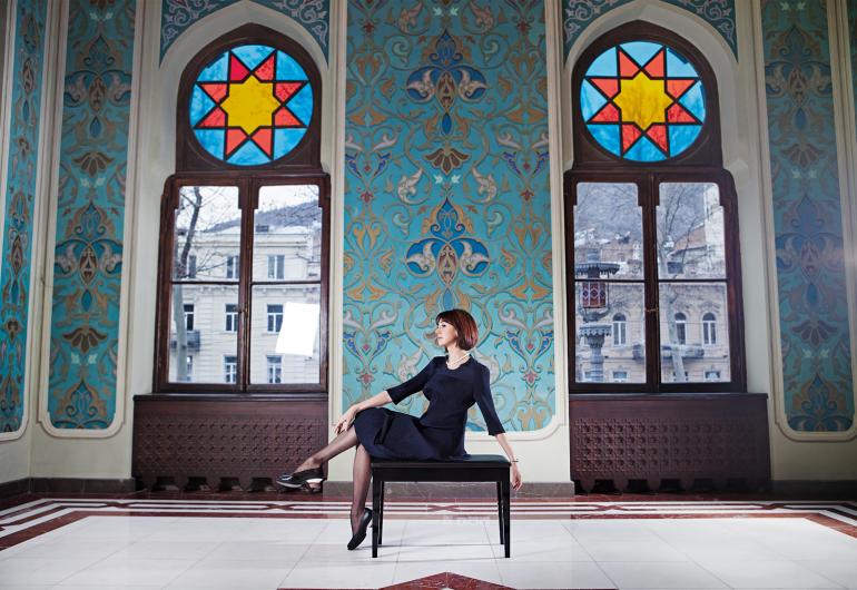 Nina Ananiashvili poses on a piano bench in an ornate room