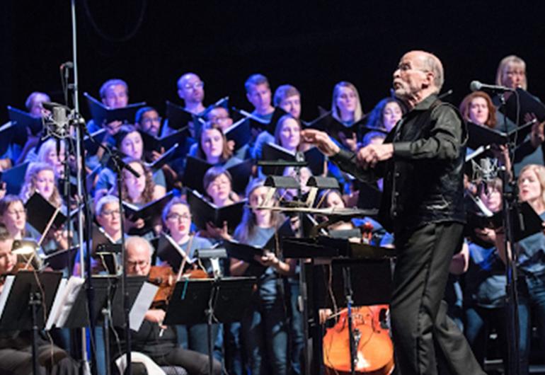 A conductor in a black shirt and pants directs an orchestra.