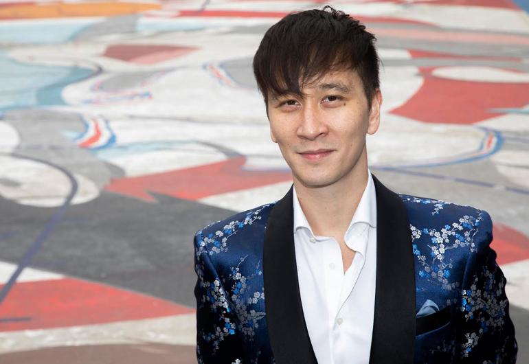 Phil Chan in a dark blue formal jacket with a colorful floor in the background