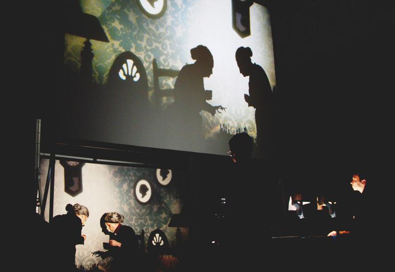 Live performance making shadow film projected on a screen above them.