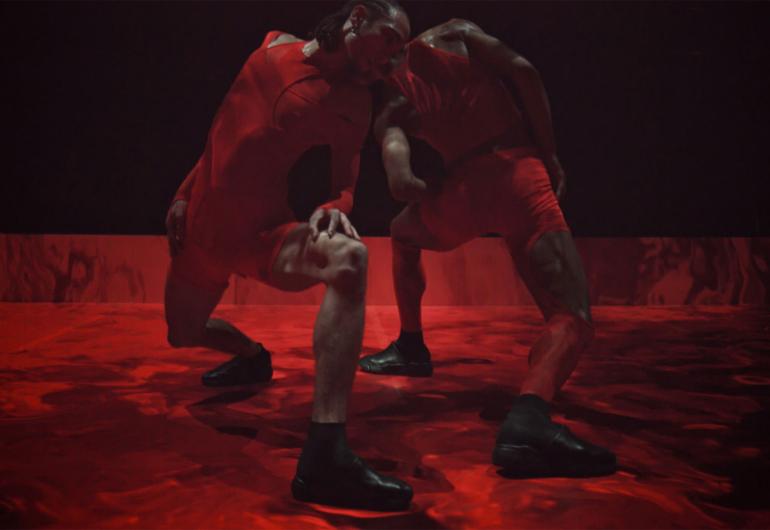 Two dancers stomp and turn in boots, on a chaotic red stage.