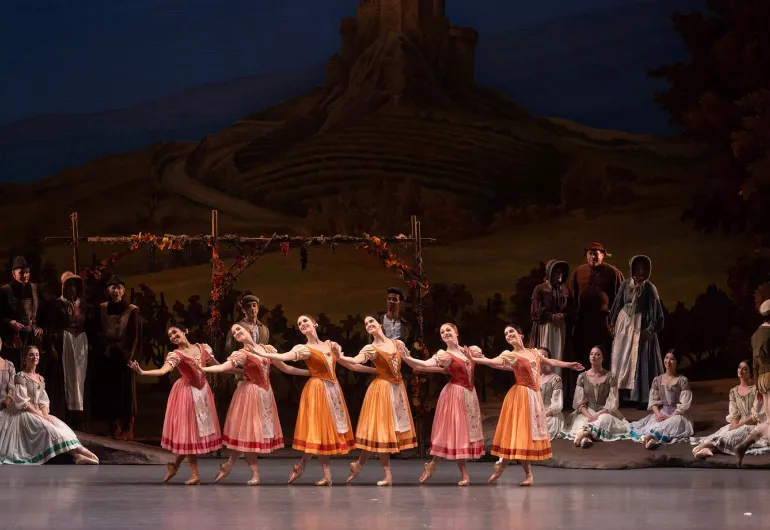 Ballerinas perform in a unison line wearing colorful villager costumes.