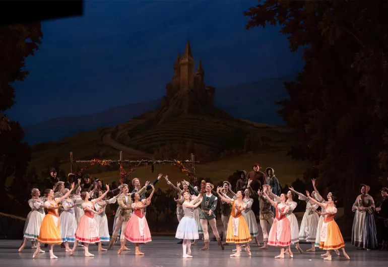 Dancers perform together on a set with a large tower in the distance.