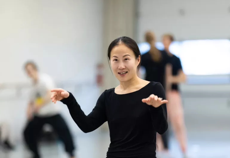 Yue Yin, a woman wearing all black, directs a choreography rehearsal.