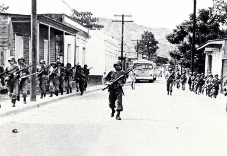 Black and white image of soldiers marching down a street in Puerto Rico.