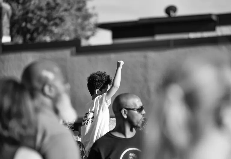 A child in white tshirt and small afro with fist raised stands out amongst a sea of blurred protesters at George Floyd Square