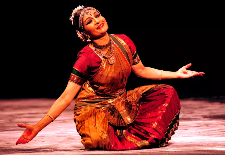 Ranee Ramaswamy smiles while she performs in sitting position, arms open to sides