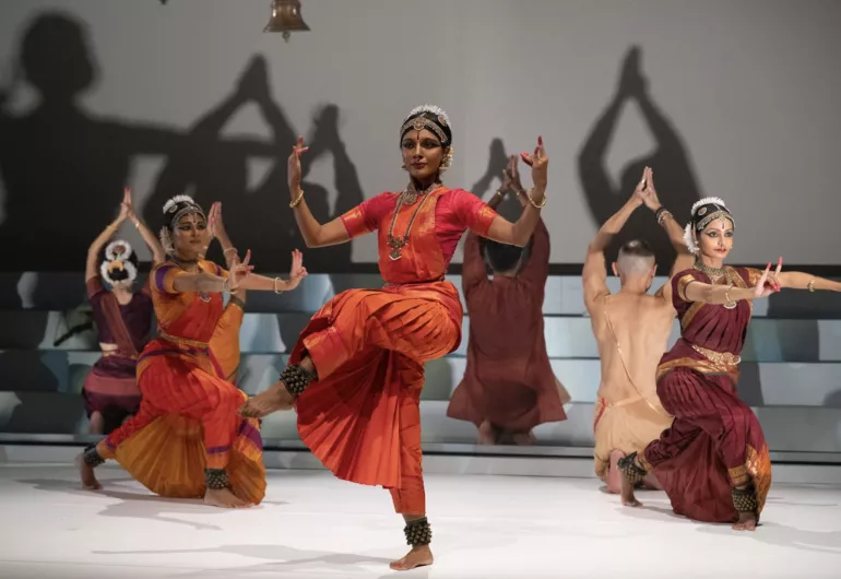 Dancers perform on white stage with shadows casting on a white wall in the background.