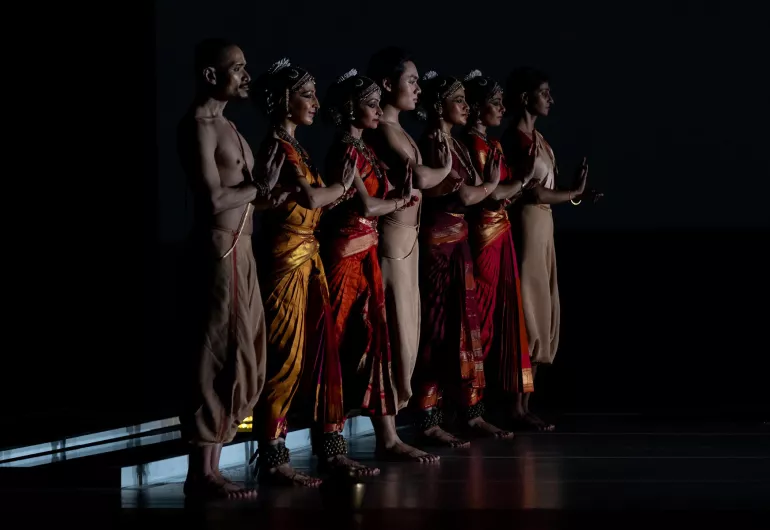 Company stands in a line facing the audience on dimly lit stage