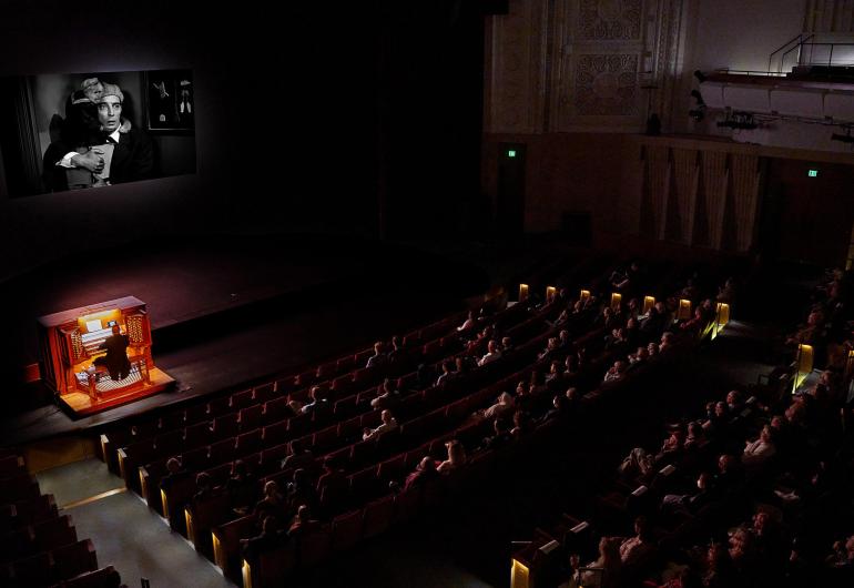 Organ plays in front of a movie screen in front of a live audience