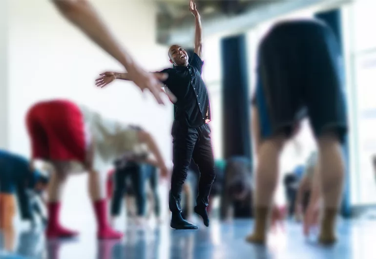 Shamel Pitts, standing with arms outstretched among a group of dancers who are bent over in a movement class.