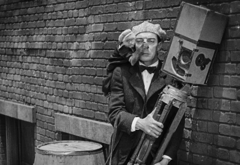 Buster Keaton with a deadpan expression. A monkey on his shoulder covers his nose.