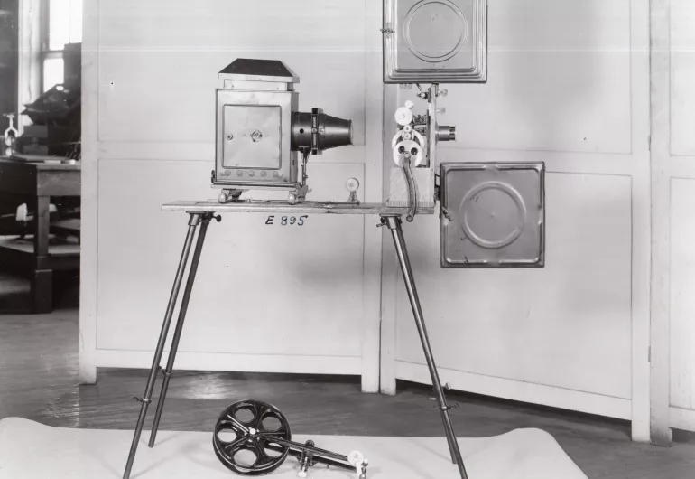 The Kinetoscope: Vintage projector equipment on a stand with an unattached reel beneath it.