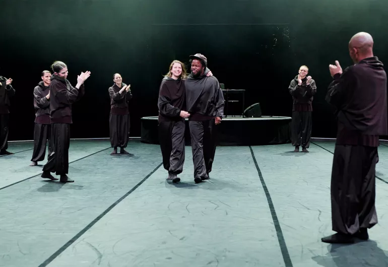Aszure Barton and Ambrose Akinmusire walk together while dancers applaud onstage.