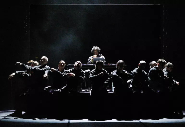 Silhouetted dancers sit in front of trumpeter Ambrose Akinmusire on a dimly lit stage.