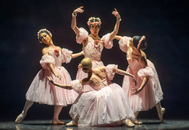 Four male dancers from the Trocks in pink dresses form an elegantly posed circle on stage. Image linked to a YouTube video.