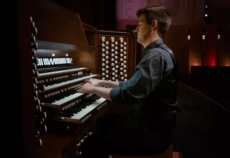 Greg Zelek, a man with short brown hair in a navy button-up, plays the pipe organ.
