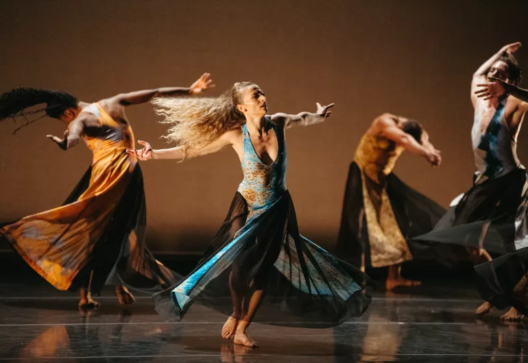 Dancers spin in circles on stage with arms open wide.