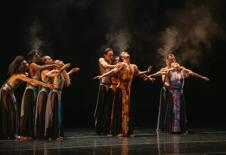 A group Martha Graham dancers form 3 lines, dancers facing the one in front the other arms reaching around or to the side.