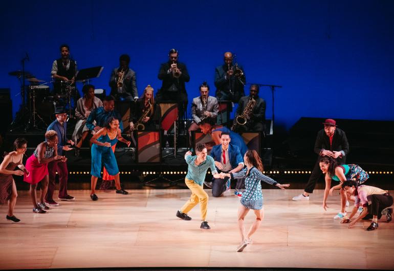 Dancers swing dance on stage with a band playing behind them