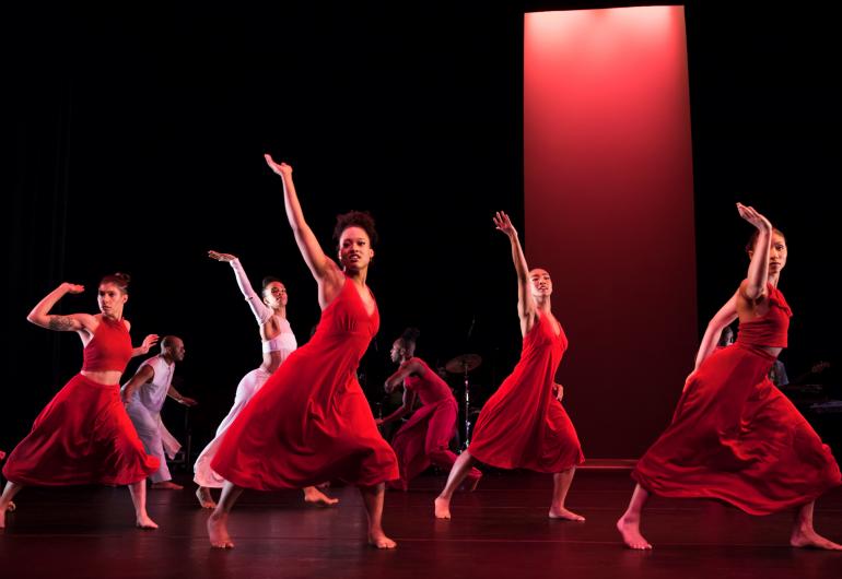 A group of dancers in red dresses perform on stage.