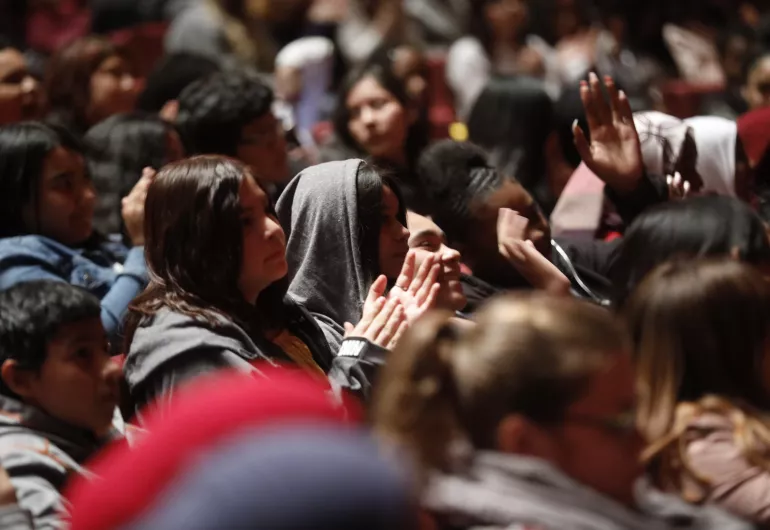 Students smiling and clapping while seated in a theater.