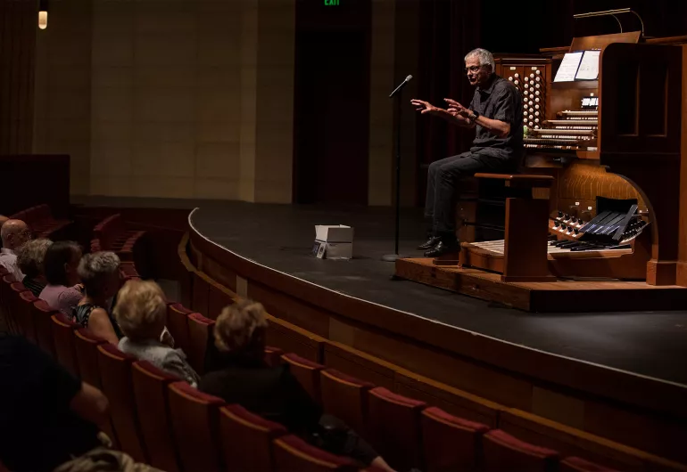 Hector Olivera sitting at the Aeolian-Skinner Opus 892 on the Northrop stage facing the audience. Olivera wears black pants and a gray shirt.