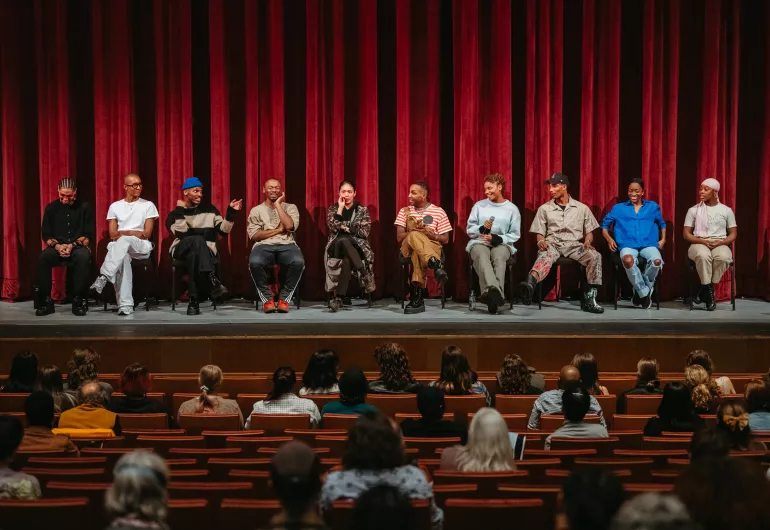 Several people sit in a row onstage and speak in front of an audience. 