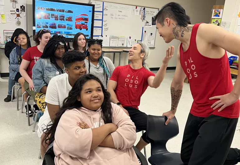 Students sit in rows in a classroom beside Pilobulus dancers in a workshop.