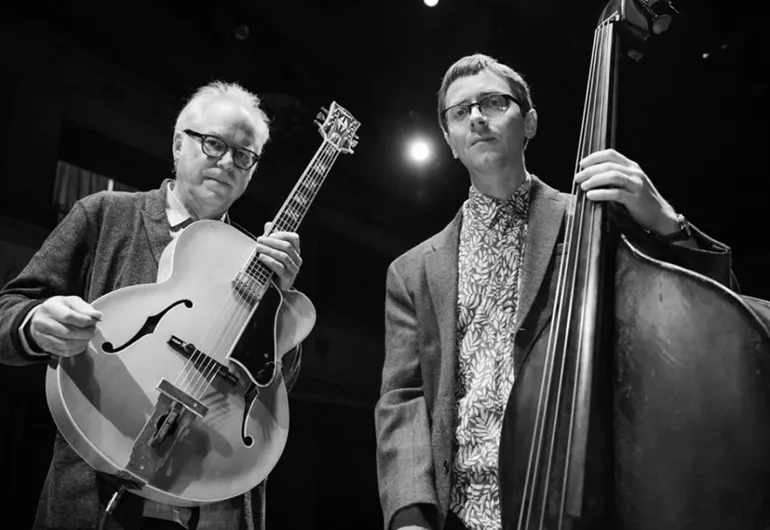 Bill Frisell holding a guitar next to Thomas Morgan holding an upright bass.