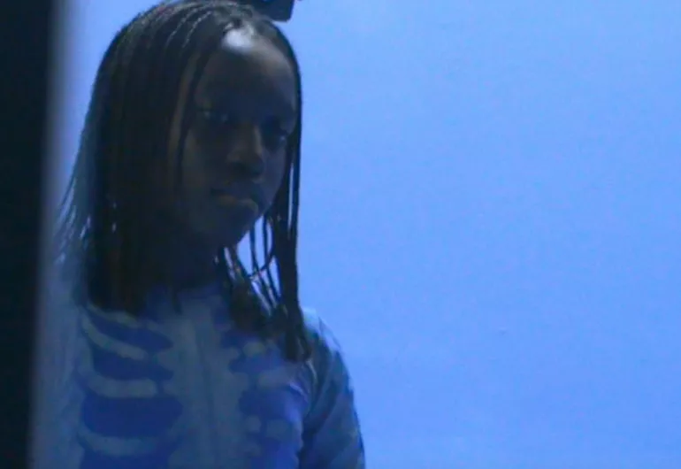 Video still of Oumy Bruni Garrel wearing a blue top with white ‘skeleton’ markings stands against a blue background.