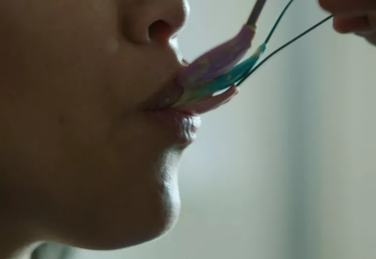 Video still close-up of a person’s mouth being fed with three different, stacked spoons at one time.
