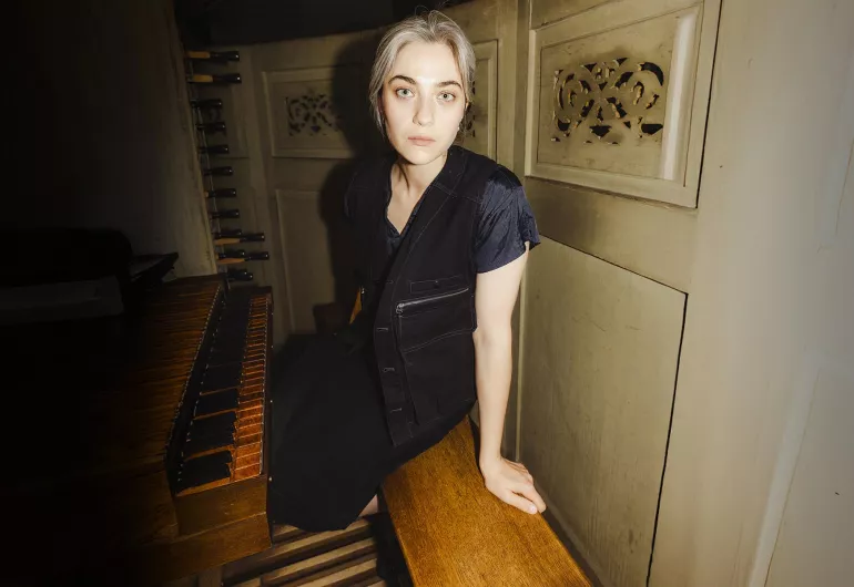 Kali Malone, a woman wearing all black, sits at the organ.