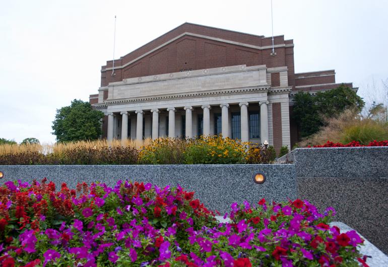 A view of the front facade of Northrop with red and purple flowers in the foreground.