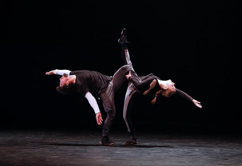 1. Two dancers stading on one foot, one holds the leg of the other while kicking up, both arching backwards with arms open