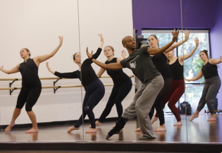A large group of dancers practicing in front of a mirror, following the moves of a member of Malpaso Dance Company.