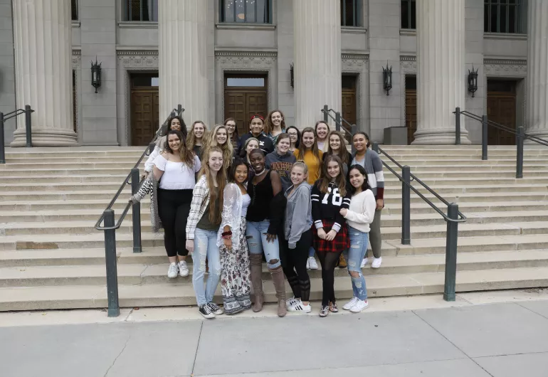 A group of teenagers stand on the stairs of Northrop smiling at the camera.