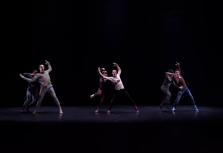Company dances in pairs, person behind holds the person in front who has their arms up and open