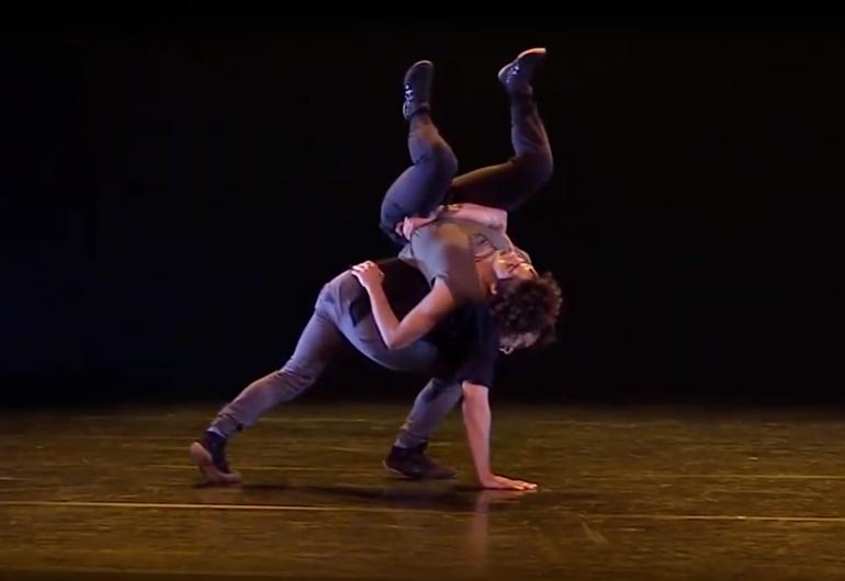 Two dancers, one lunges with a hand on the floor, the other is one their back with her legs up in the air