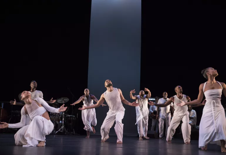 A group of dancers wearing all white perform on stage.