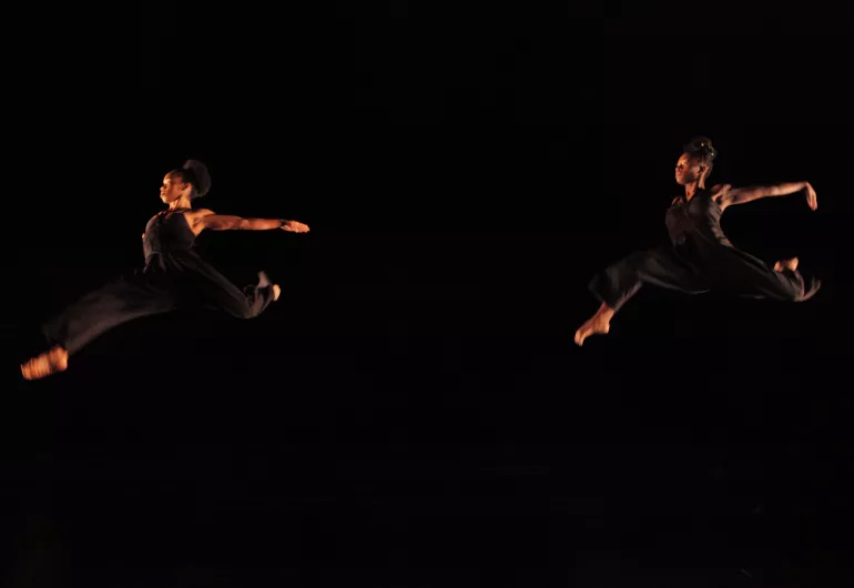 Two dancers leap high in the air with their leg spread wide.