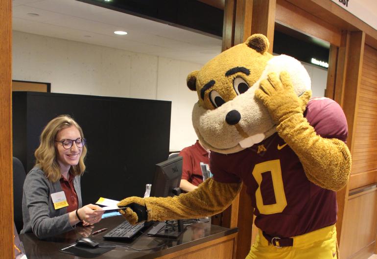 Goldy Gopher taking a ticket from a worker in the Northrop ticket booth.
