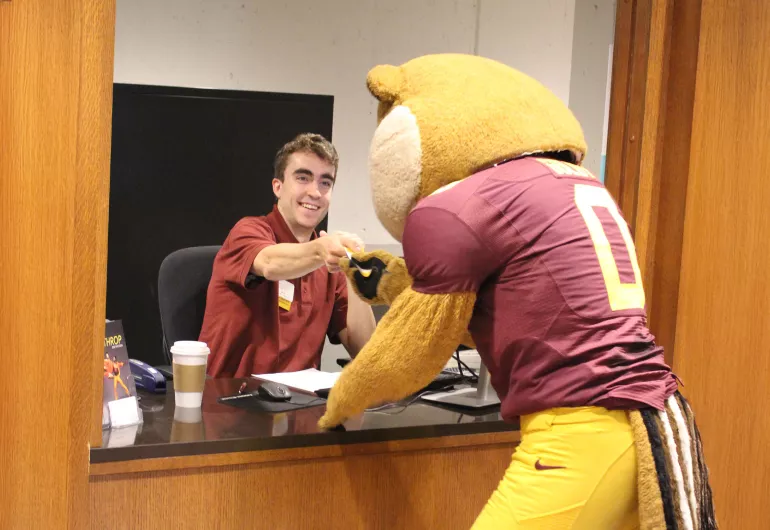 Goldy Gopher taking a ticket from a worker in the Northrop ticket booth.