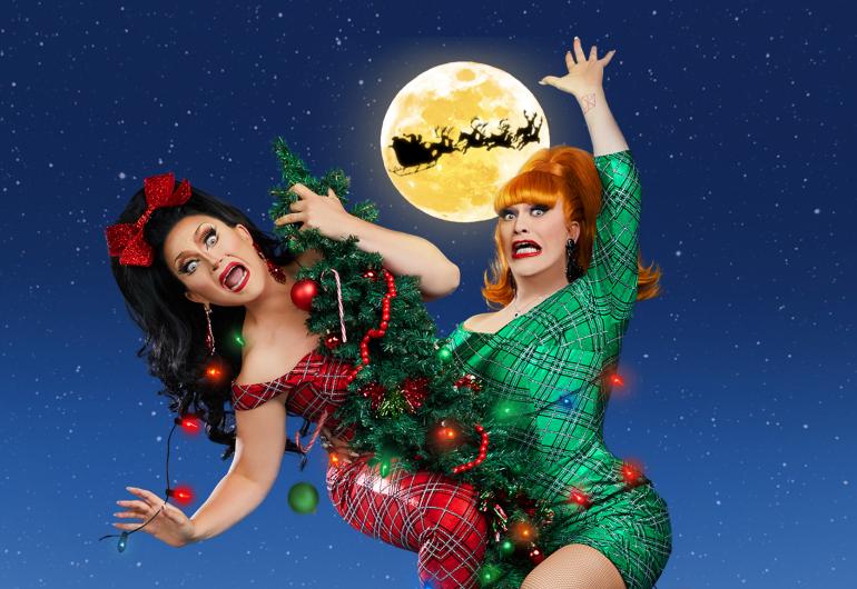 Drag Queens BenDeLaCreme and Jinkx Monsoon dressed in red and green dress are comically tangled in the decorations of a Christmas tree.