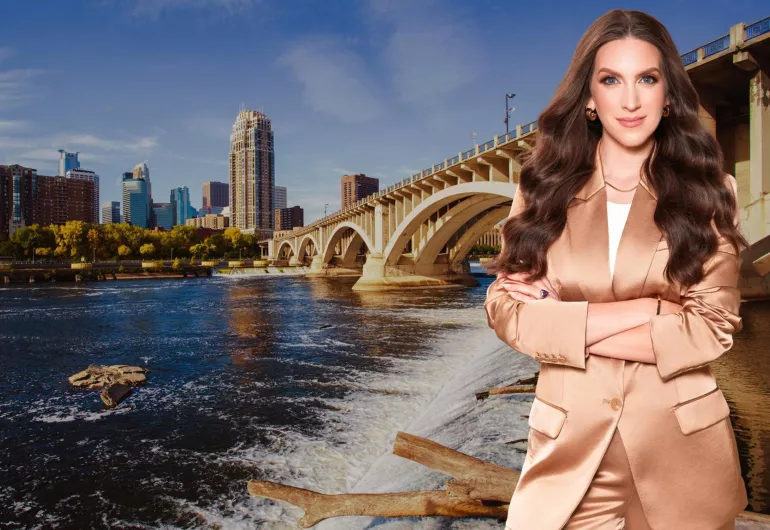 Minneapolis Urban riverfront scene with a bridge, city skyline, and a person in a light brown suit in the foreground.