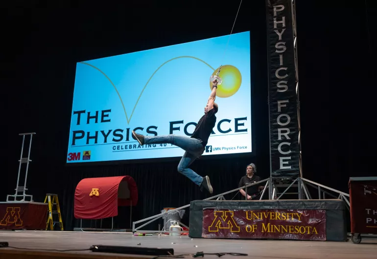 A man swings over the stage on a trapeze.