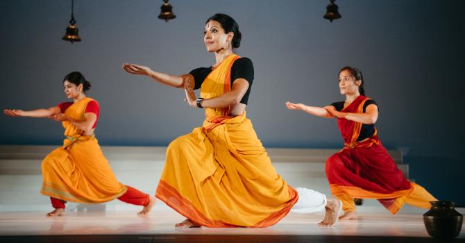 Three dancers in red and yellow pose on stage.